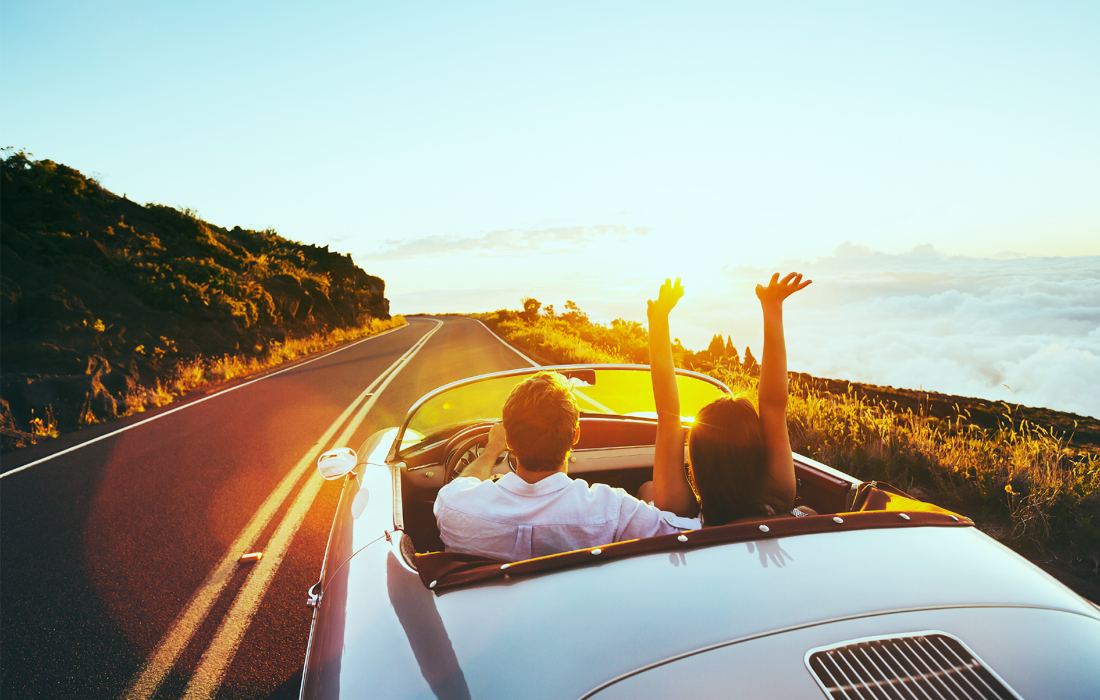 オープンカーで海沿いの道を走るカップル